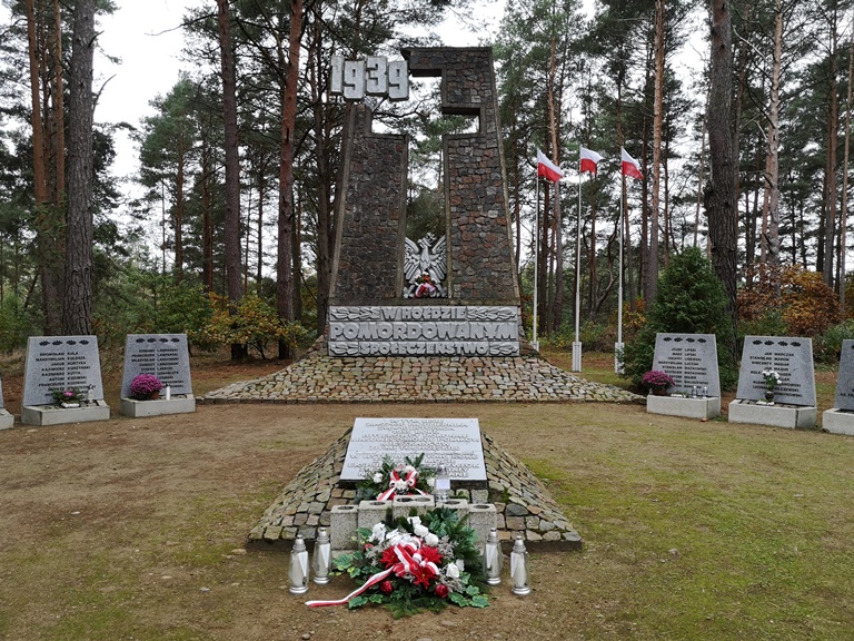 Znicze i wiązanki kwiatów przy Pomniku Pomordowanych w lesie w Rudzkim Moście